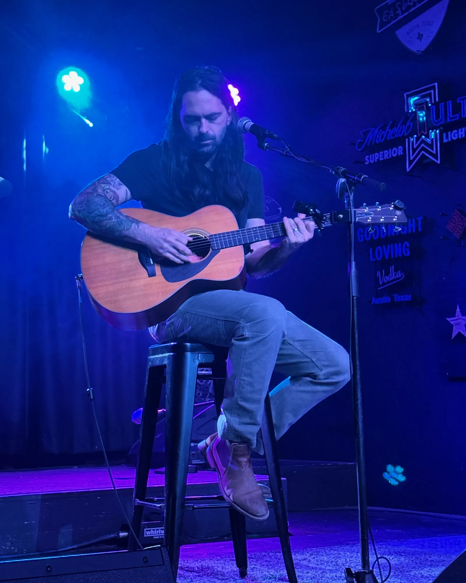 Justin Boyson performing solo with an acoustic guitar under blue stage lights